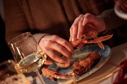 Person skalar bohuslänsk kräfta och dricker vitt vin.